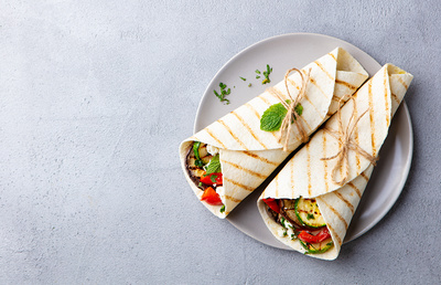 Wrap sandwich with grilled vegetables and feta cheese on a plate. Grey background. Copy space. Top view.